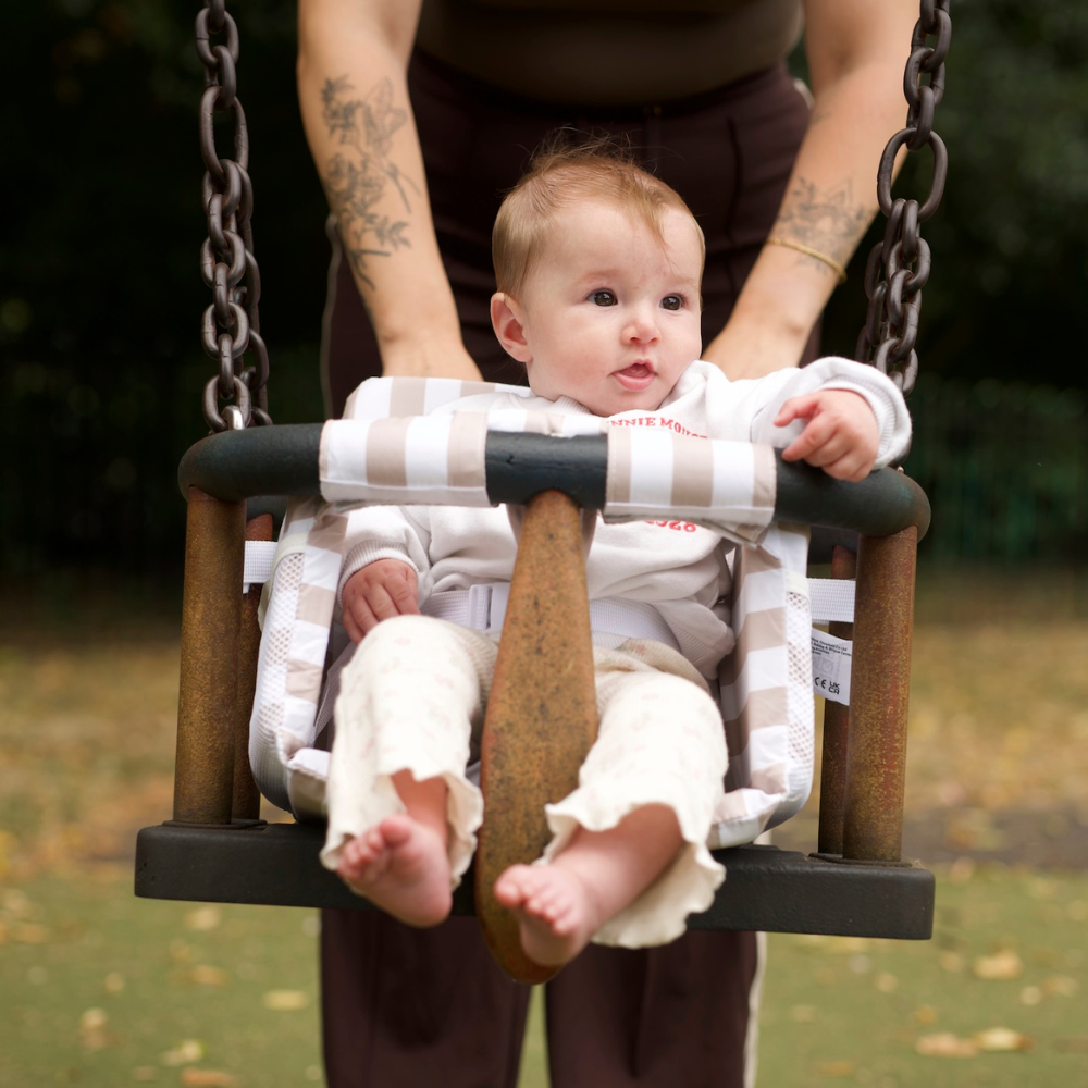 Baby sitting in a park swing with the Little Sonny seat