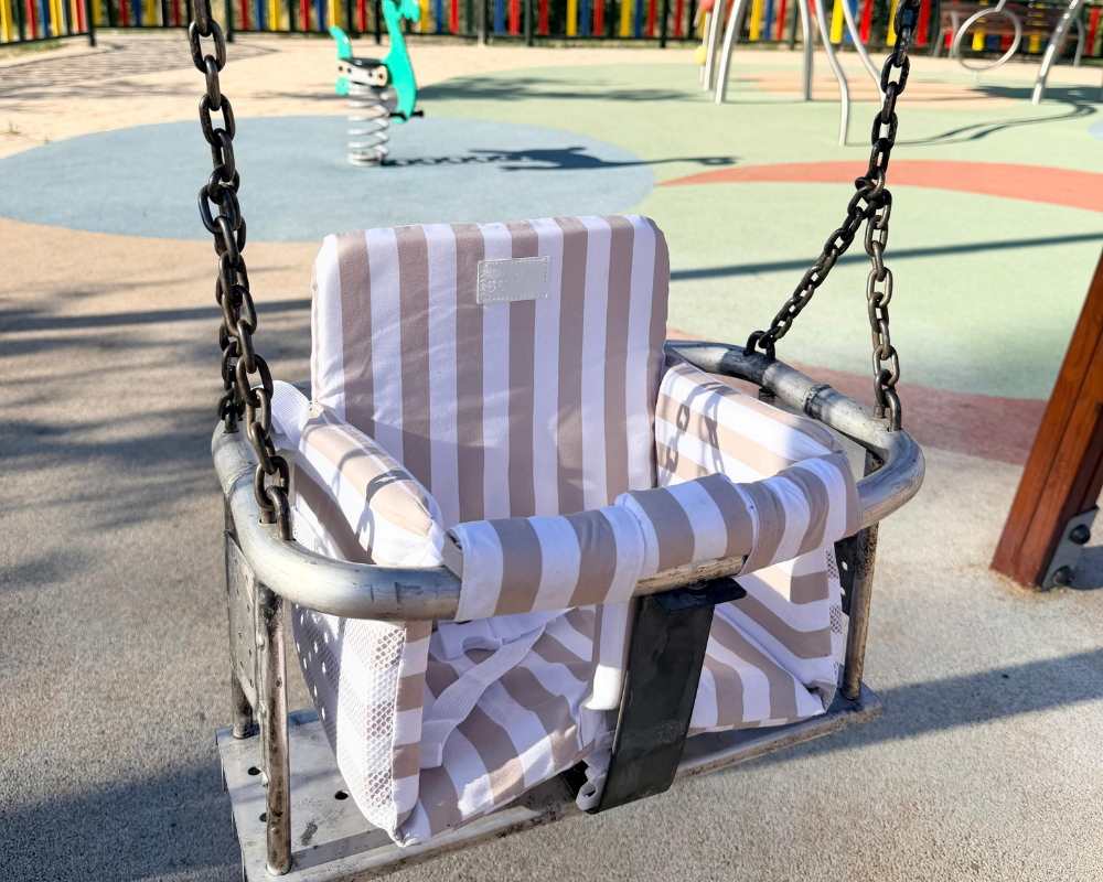 Toddler seated in a park swing with a sand Little Sonny seat insert